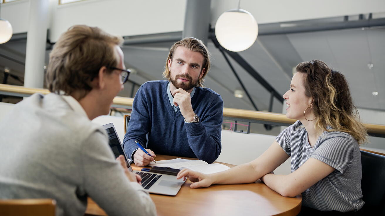 Tre personar i samtale rundt eit bord.