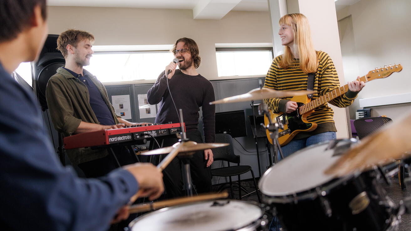 Studenter som spiller og synger i et studentband i et øvingslokale